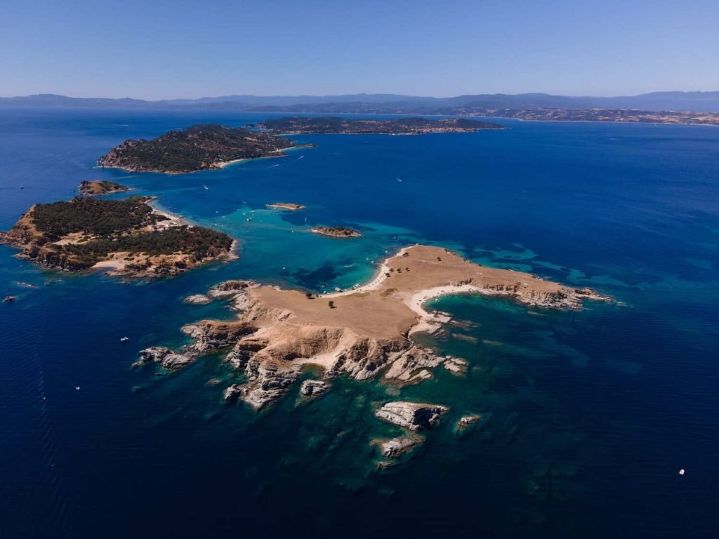 Aerial view of Drenia Island near Ouranoupoli — white sand beach surrounded by crystal-clear turquoise Aegean waters, Halkidiki
